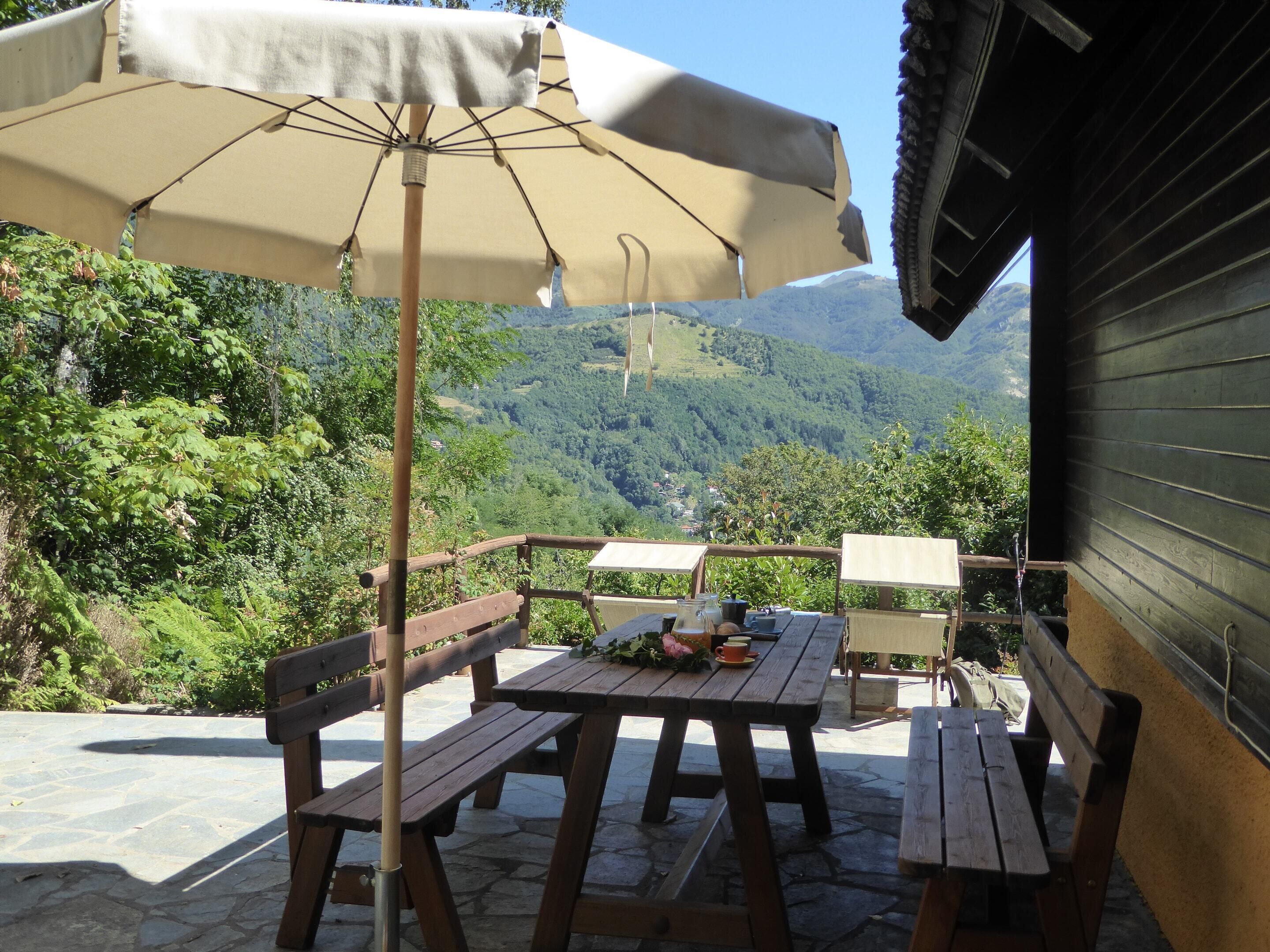 A patio with wooden benches and tables, an umbrella, and a view of a mountainous landscape.