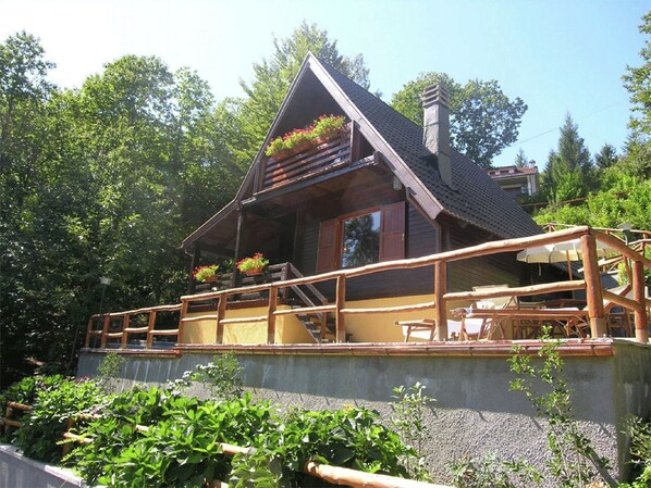 A wooden cabin with a balcony, surrounded by greenery.