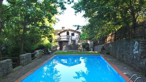 Ein rechteckiger Swimmingpool mit Steinbord, umgeben von einer Steinmauer und einem Holzzaun.