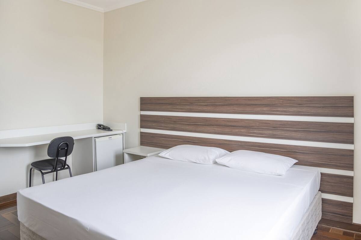 Une chambre à coucher comprenant un lit, une table de chevet, une chaise et un bureau avec un téléphone et un petit réfrigérateur.
