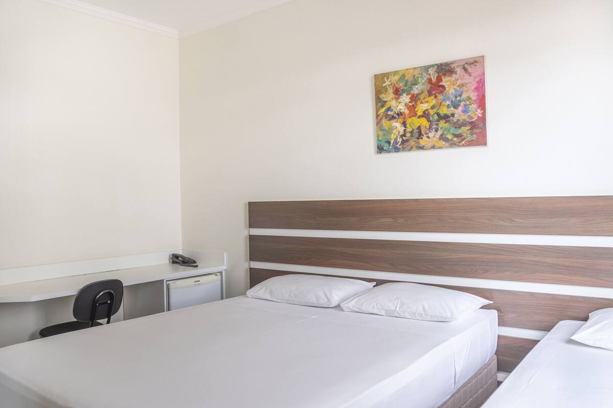 Une chambre d’hôtel avec un grand lit, un bureau avec un téléphone et un tableau abstrait aux couleurs vives accroché au mur.