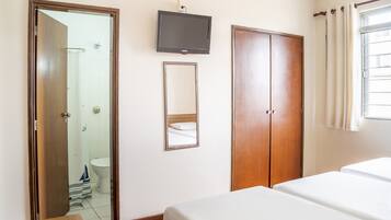 Quarto de hotel com guarda-roupa de madeira, televisão na parede e cama com roupa de cama branca.