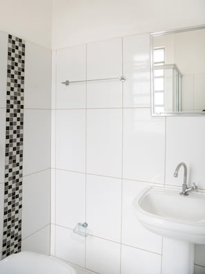 A bathroom with white tiled walls, a black and white checkered tile accent, a metal towel rack, a sink, and a mirror.