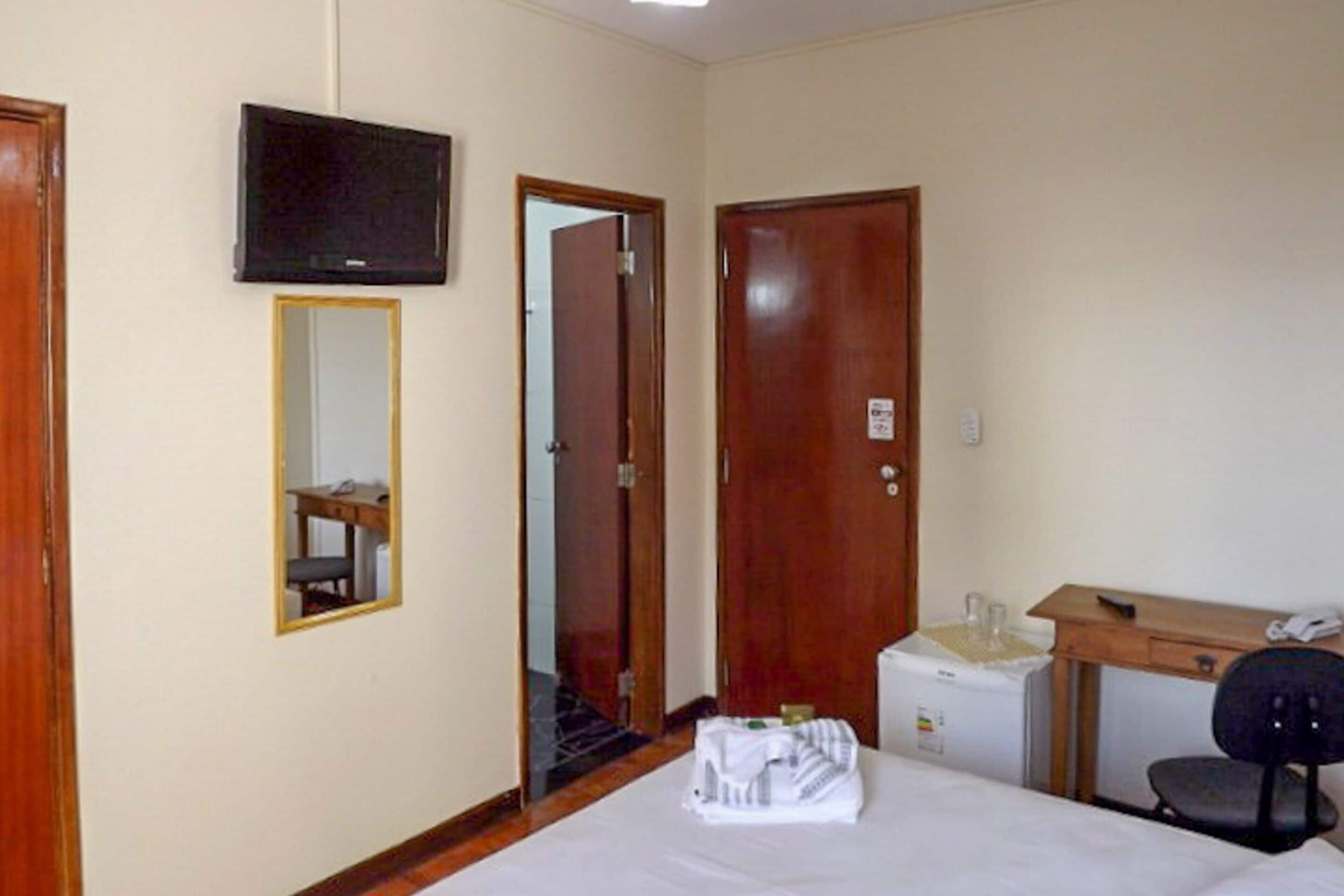 Een hotelkamer met een bed, een bureau, een stoel, een televisie en een spiegel.