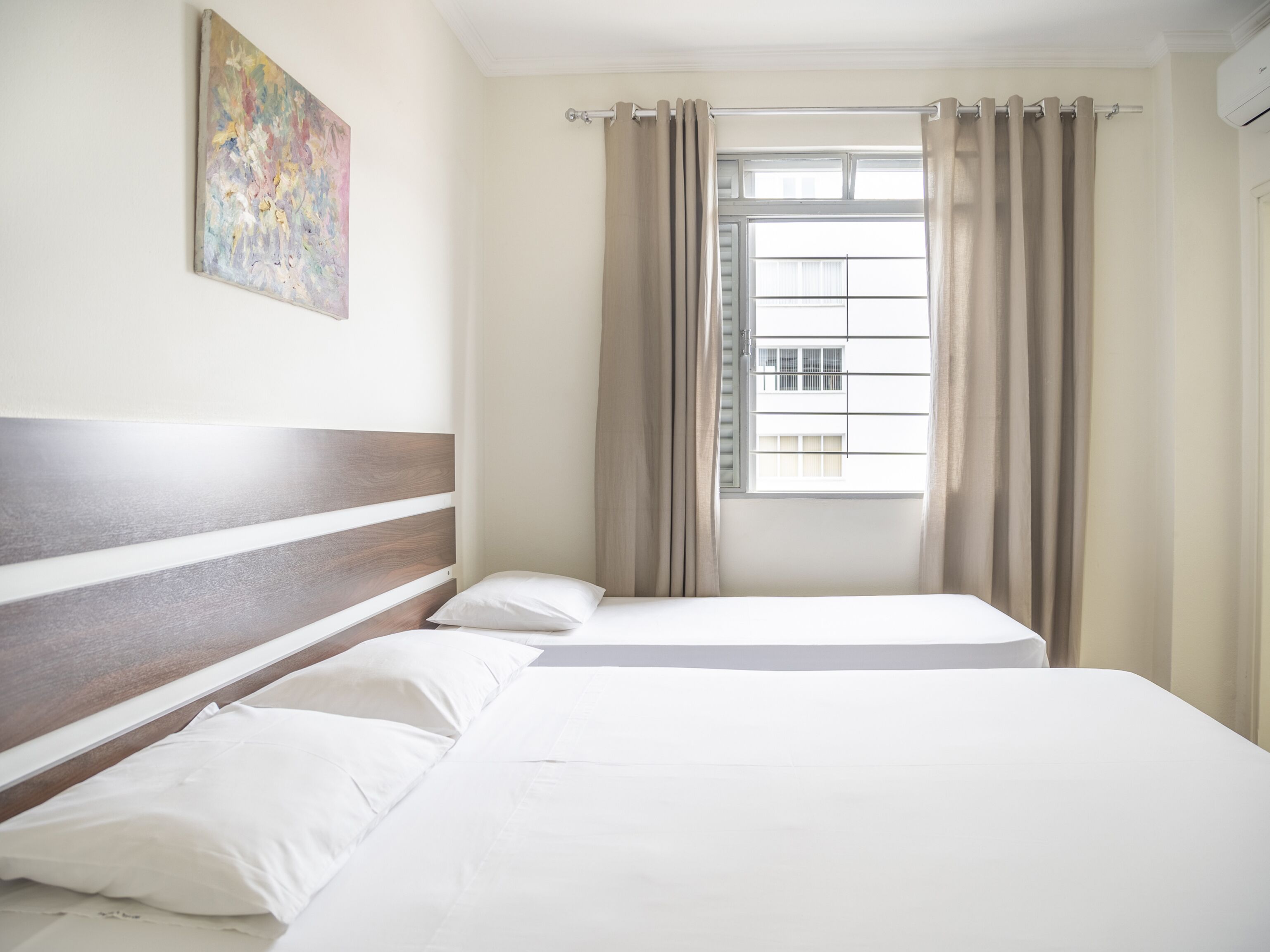 A hotel room with a bed, a window with curtains, and a painting on the wall.