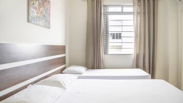 A hotel room with a bed, a window with curtains, and a painting on the wall.