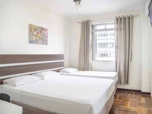 A hotel room with a large bed, a small desk, a window with curtains, and a colorful painting on the wall. - Libero Hotel (Sao Joao da Boa Vista)