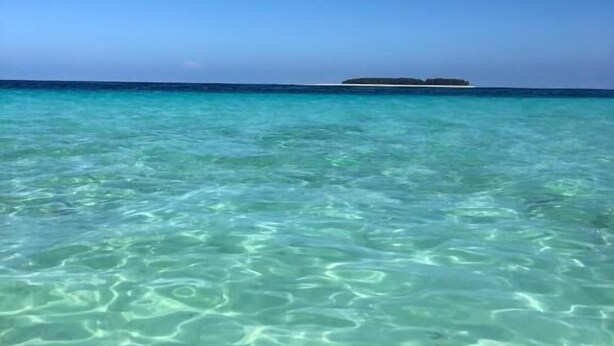 Een helder uitzicht op een strand met turquoise water en een klein eiland in de verte.