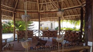 Een overdekt terras met houten meubels en hangplanten.