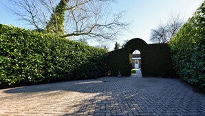 A paved pathway leading to a building through a hedge.