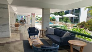 Eine Lounge mit einer Couch, Sesseln und einem kleinen Tisch mit Blick auf einen Pool und Grünflächen.