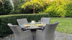 Un tavolo rotondo all'aperto con sedie in vimini, su un patio in pietra circondato dal verde.