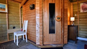 Una baita di legno con sauna, una sedia bianca e un tavolino con una lampada.