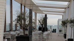 An outdoor seating area with white wicker chairs and tables, a wooden deck, and a view of the sea. - Beautiful Villa Near the Beach of Cadzand (Cadzand-Bad)