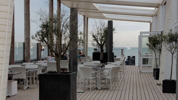 Un espace extérieur aménagé avec des chaises et des tables en osier blanc, une terrasse en bois et une vue sur la mer.