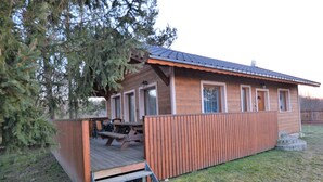 A wooden cabin with a covered patio, a wooden deck, and a fenced yard.
