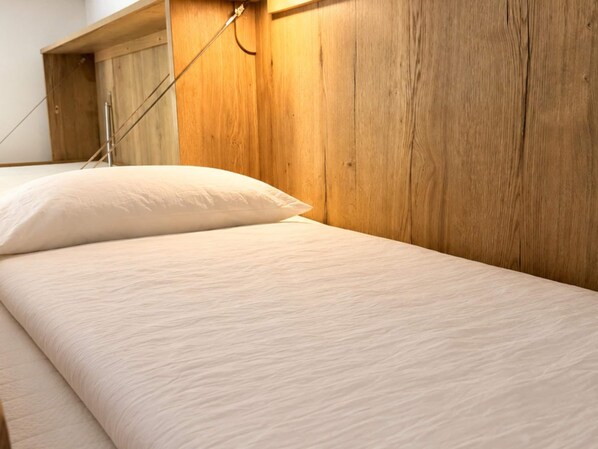 Una cama con cabecera de madera, almohada blanca y estructura metálica de soporte.