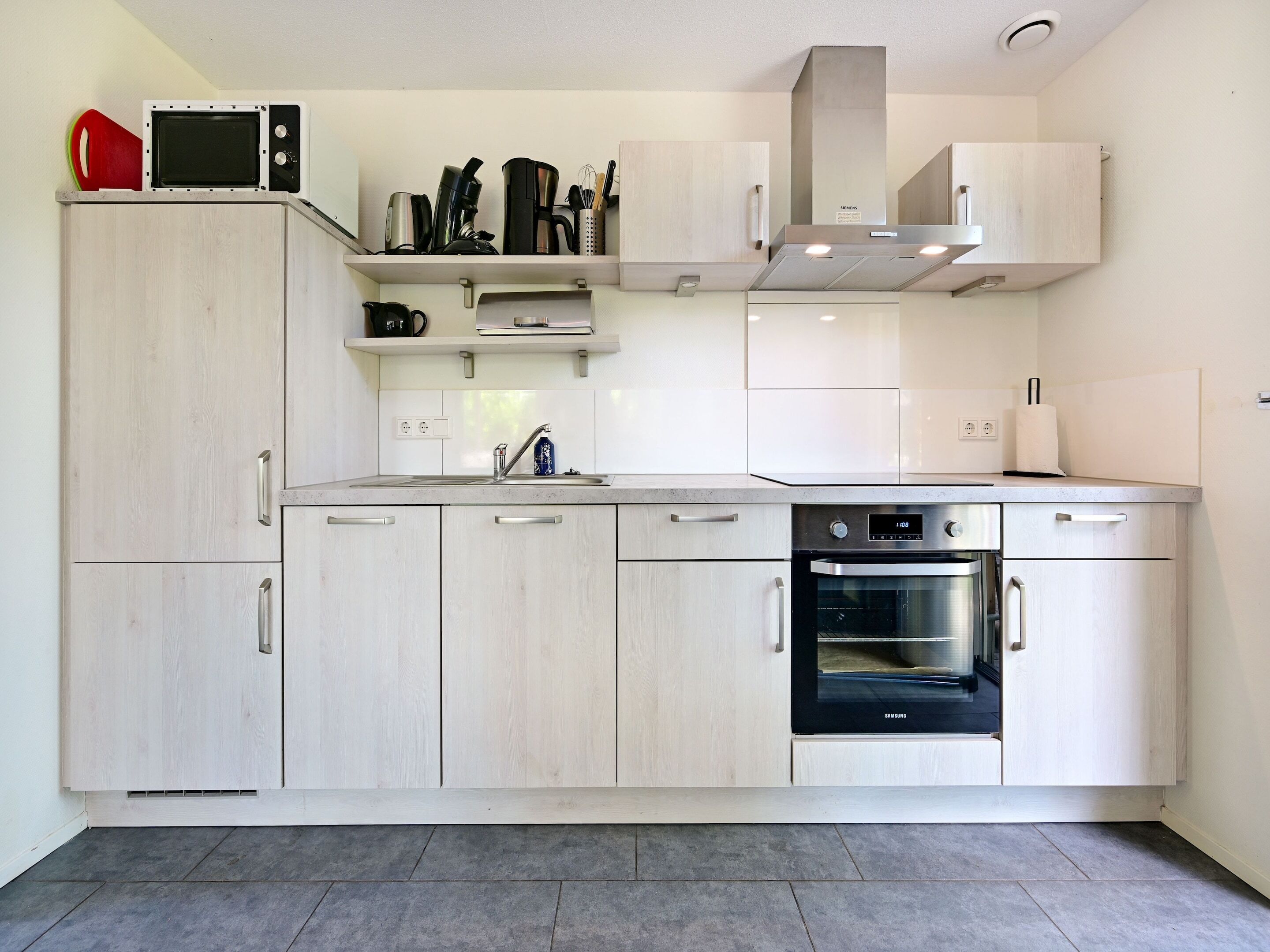 A modern kitchen with light wood cabinets, a built-in oven, and stainless steel appliances.