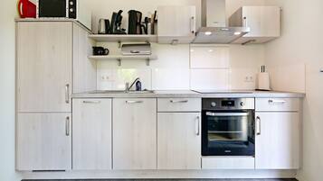A modern kitchen with light wood cabinets, a built-in oven, and stainless steel appliances.