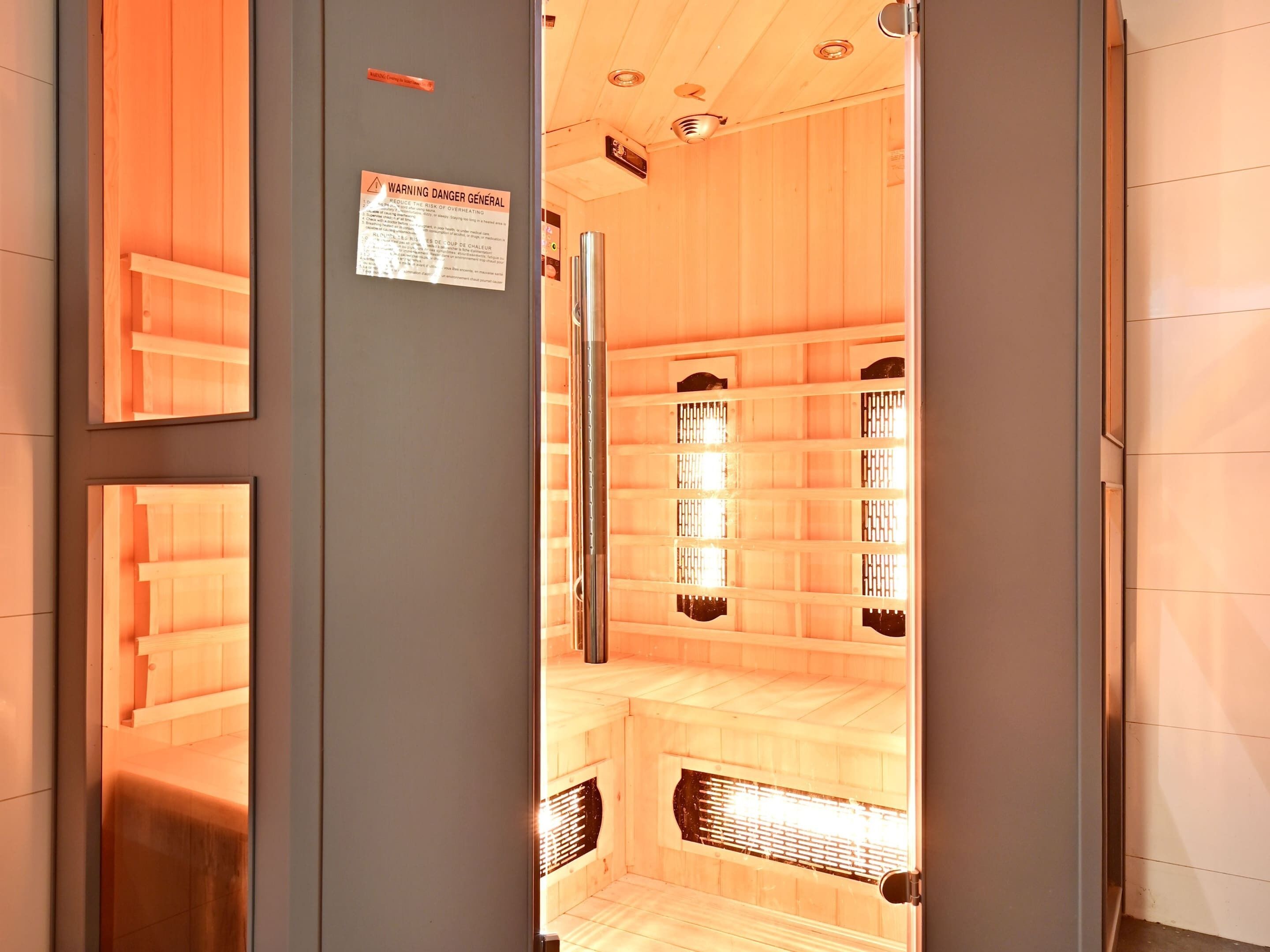 A sauna room with wooden walls and benches, a visible warning sign, and a ventilation system.