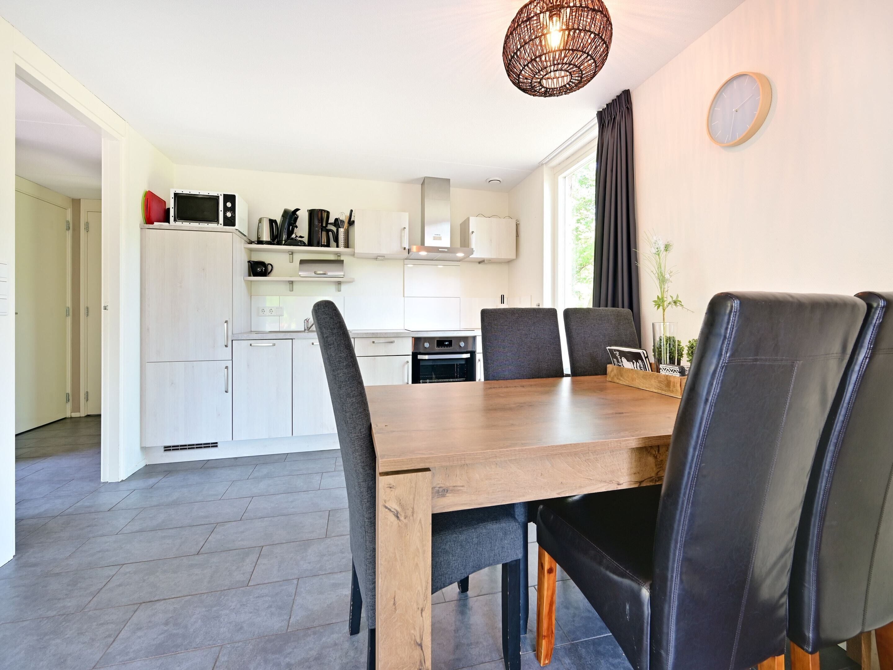 Une cuisine moderne avec des meubles blancs, une table à manger en bois et des chaises noires.