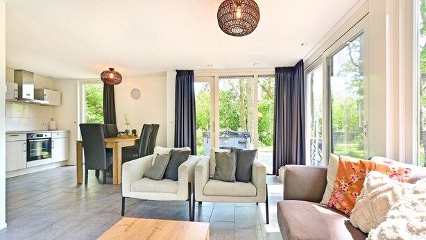 Ein modernes Wohnzimmer mit Sofa, Sesseln und Couchtisch. Es gibt eine Essecke mit Tisch und Stühlen sowie eine Küche im Hintergrund.