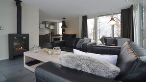Ein modernes Wohnzimmer mit Kamin, einer Couch, einem Couchtisch und Blick auf die Küche sowie nach draußen.