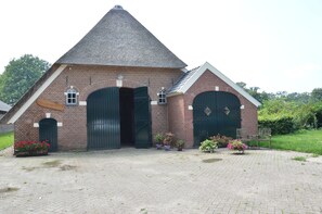 A brick building with a conical roof, two large doors, and potted plants in front. - Farmhouse in Geesteren Near Golf Course (Geesteren)