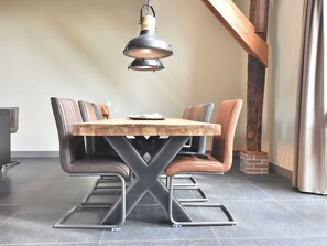 A dining area with a wooden table, cushioned chairs, and a hanging industrial-style light fixture. - Grandeur Farmhouse in Dwingeloo at a National Park (Dwingeloo)