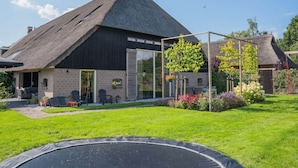 Ein Haus mit Strohdach, Backsteinfassade und einem Garten mit Trampolin.