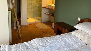 A bedroom with a bed, a wooden nightstand, a green wall, a bathroom with a glass shower, and a wooden floor. - GITE DE LA BRETAUDERIE 6/8 PEOPLE NEAR ANGERS (RIVES DU LOIR EN ANJOU)