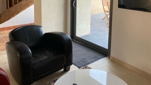 A room with a black leather chair, a white table, a TV mounted on the wall, a wooden staircase, and a sliding glass door leading outside. - GITE DE LA BRETAUDERIE 6/8 PEOPLE NEAR ANGERS (RIVES DU LOIR EN ANJOU)