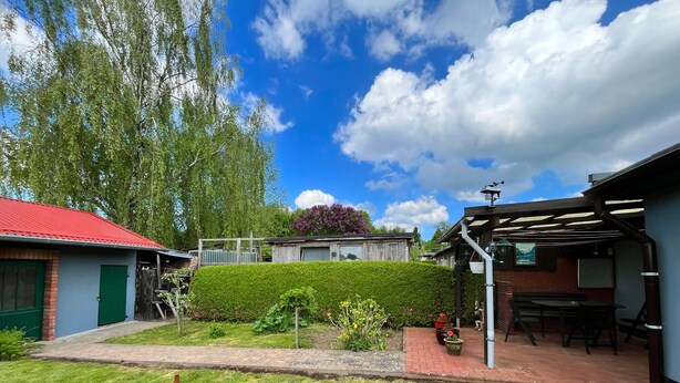 A residential property with a red-roofed house, a well-maintained garden, and a patio area with outdoor furniture. - Hubsches Appartement in Kropelin mit Terrasse (Kroepelin)
