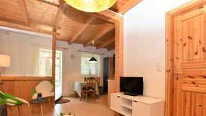 A cozy room with a wooden ceiling, a dining area with a table and chairs, a television on a white stand, and a large wooden door. - Cozy Apartment in Rerik near Sea (Rerik)