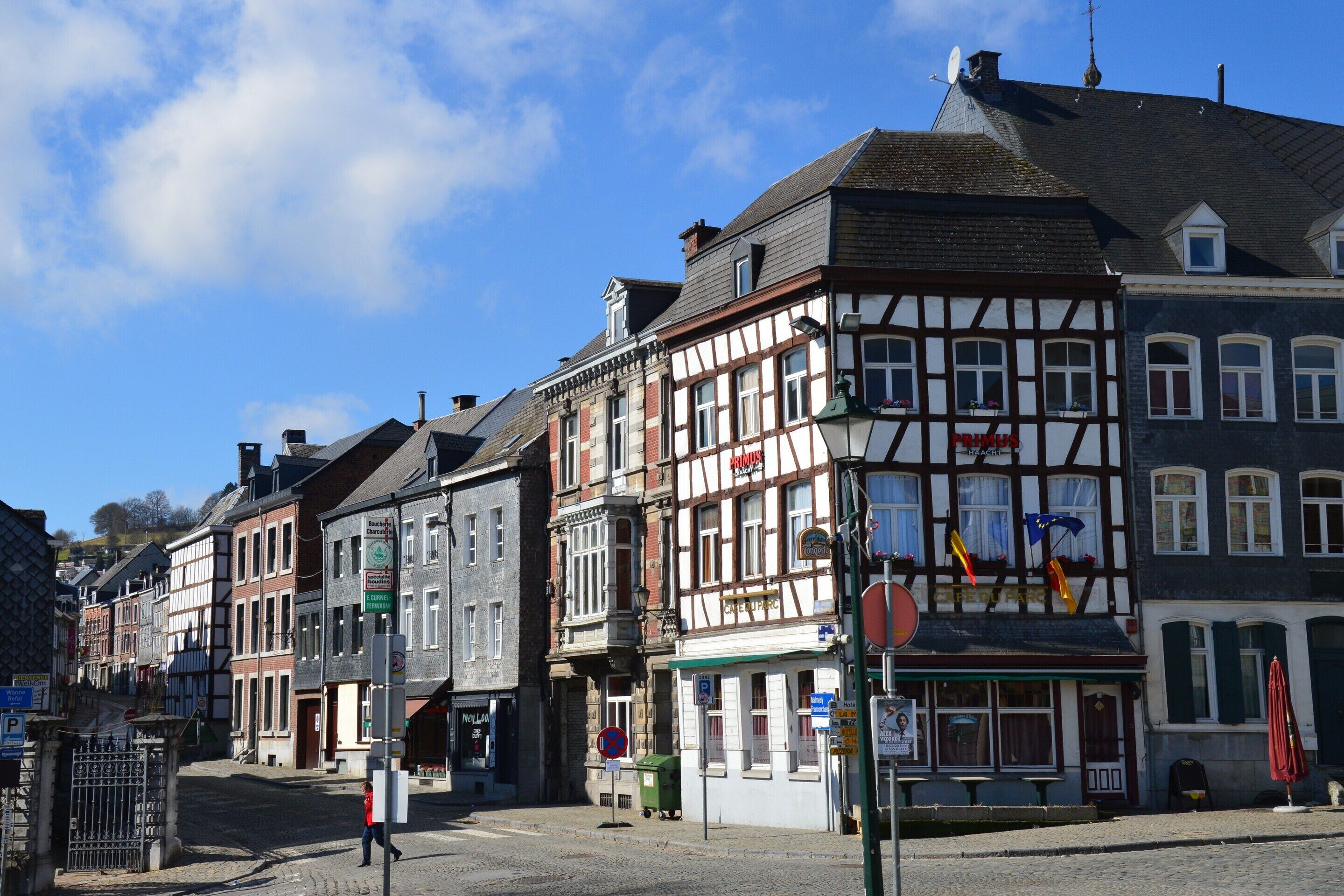 Une rangée de bâtiments traditionnels à colombages, bordée d’une rue pavée, avec un passage piéton et un petit kiosque.