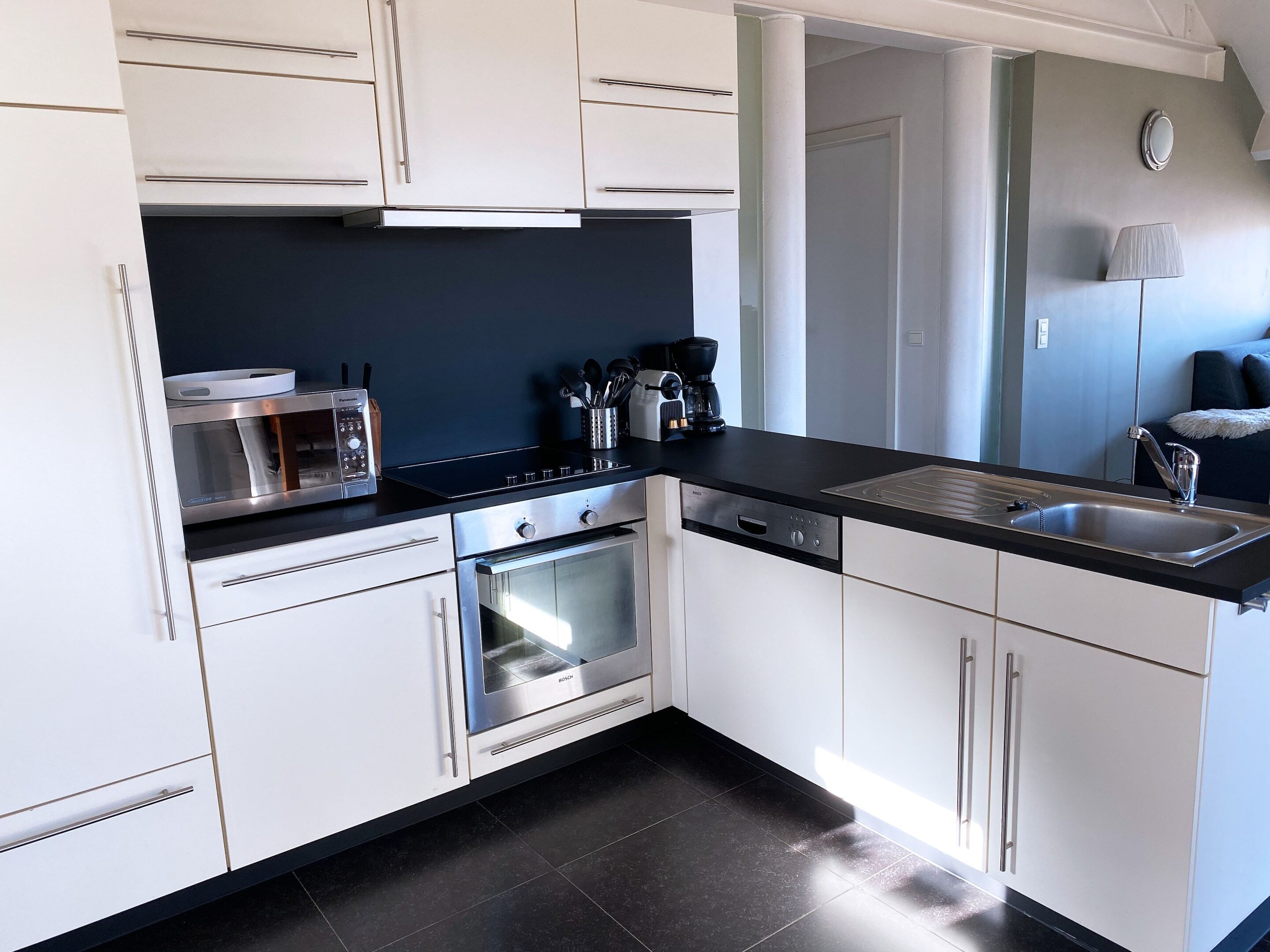 A modern kitchen with white cabinets, a Bosch oven, a coffee maker, and a sink.