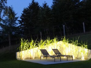 Un jardín con dos tumbonas y un muro de plantas altas.