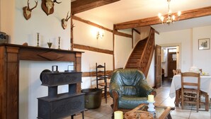 Ein rustikales Interieur mit freiliegenden Holzbalken, einem Ledersessel, einem traditionellen Ofen und einer Treppe.