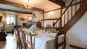 Ein Essbereich mit Tisch für vier Personen, Holzsesseln, einer Chandelüster und einer Treppe.