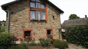 A stone building with a sloped roof, two windows with shutters, and a small porch area.