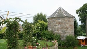 A stone tower with a conical roof, surrounded by a garden with various flowering plants and a small wooden structure.