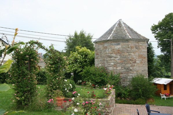 A stone tower with a conical roof, surrounded by a garden with various flowering plants and a small wooden structure.
