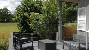 Un patio cubierto con mobiliario exterior, vista a un campo verde y un arbusto grande.