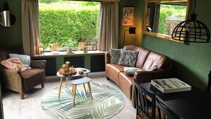 A cozy living room with a leather sofa, a small round table, and a window with curtains. - Chalet With Balcony in Veluwe (Garderen)