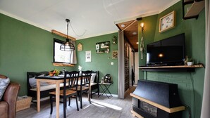 A cozy living room with a dining area, a TV mounted on the wall, and a fireplace. - Chalet With Balcony in Veluwe (Garderen)