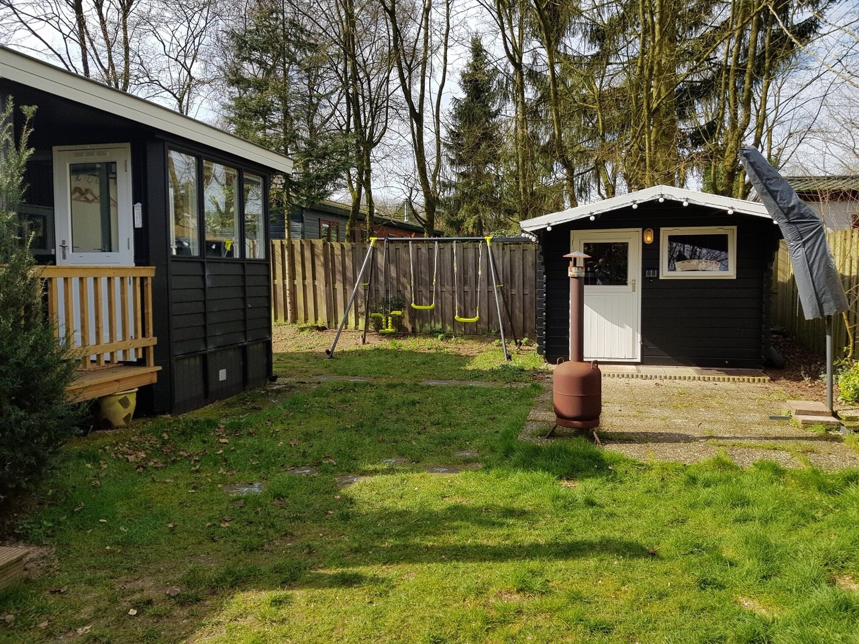 Une petite cabane avec une véranda et un abri de jardin, située dans une zone boisée.