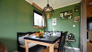 A dining area with a wooden table and chairs, a hanging light fixture, and a window with curtains. - Chalet With Balcony in Veluwe (Garderen)