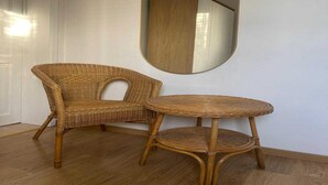 A wicker chair and a small round table in a room with a wooden floor and a white wall. - Sunny Cottage With Pool (Yvoir)