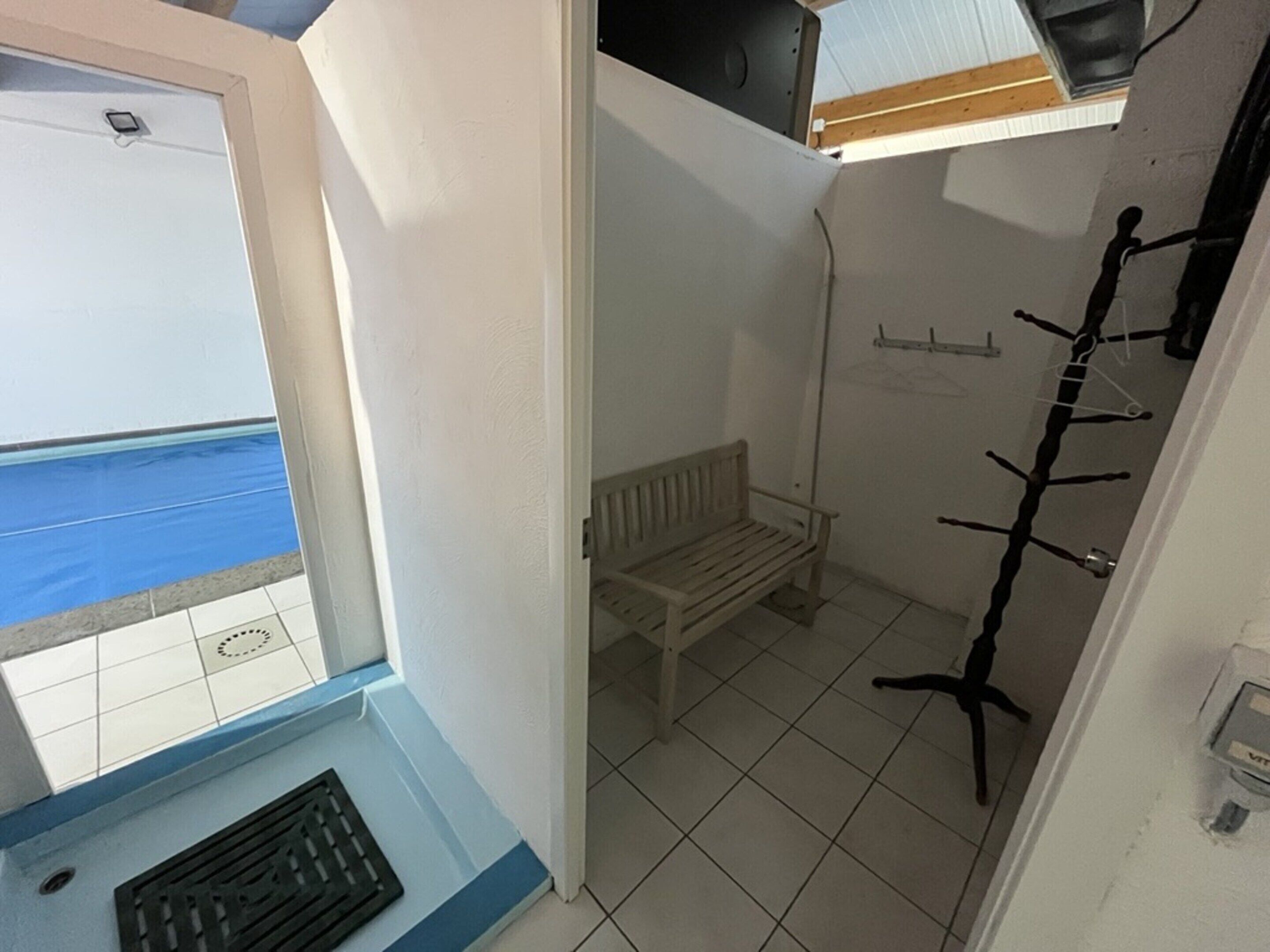 Une chambre avec une fenêtre donnant sur une piscine, un banc et un espace douche.