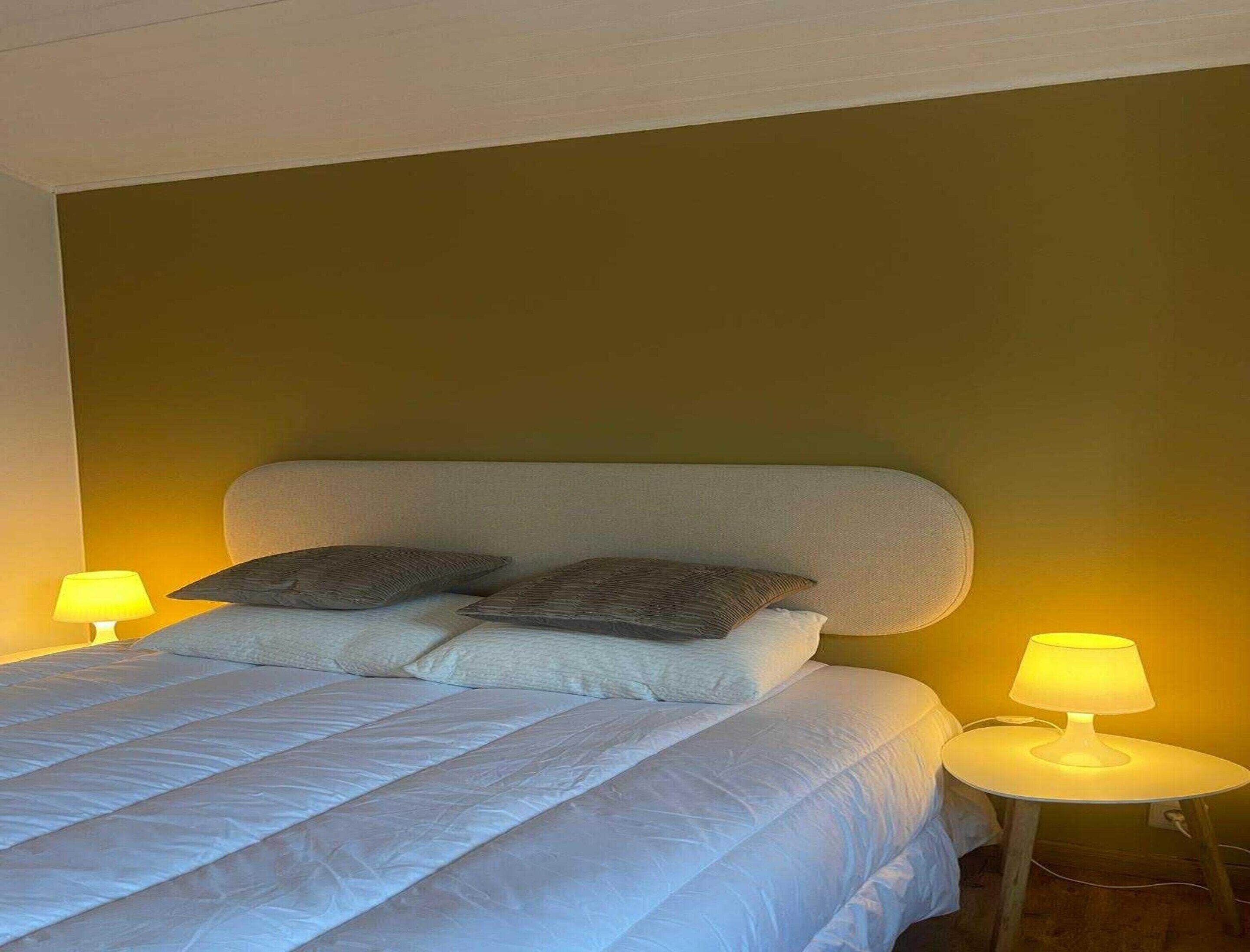 A neatly made bed with two pillows and two bedside lamps.